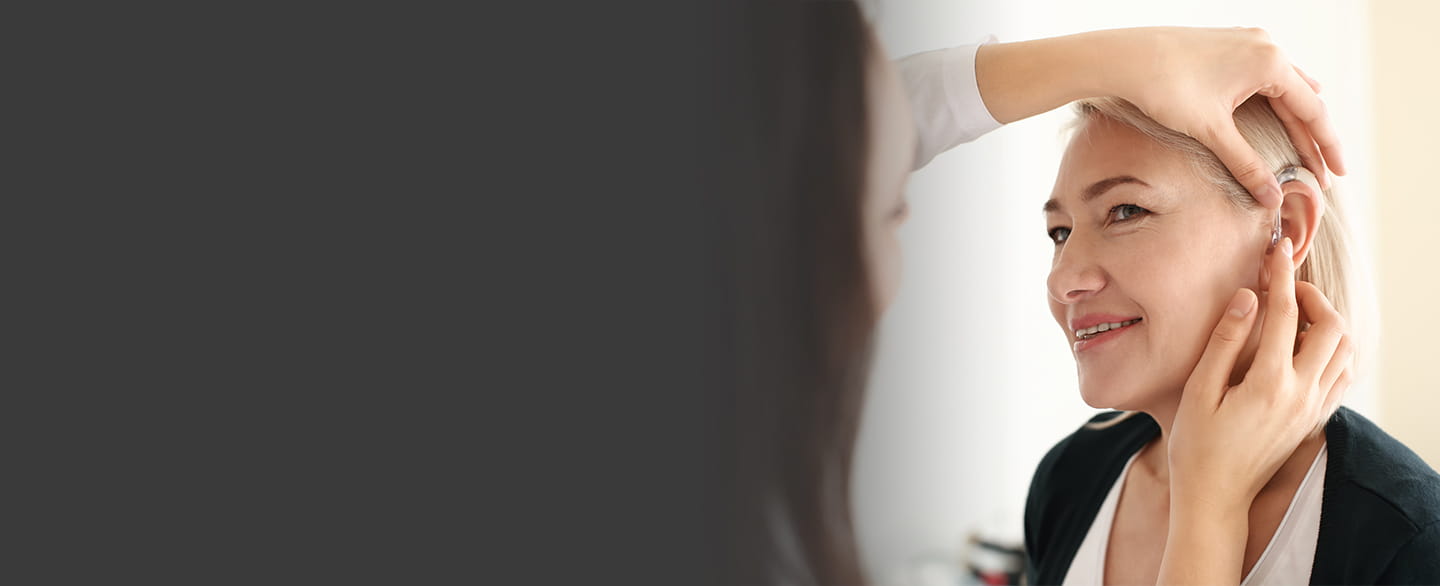 Doctor adjusting woman's hearing aid.